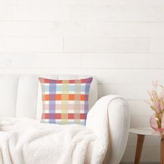 a white couch sitting next to a table with a vase on it and a plaid pillow