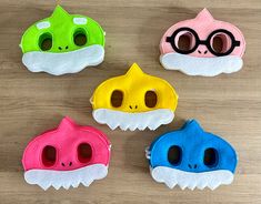 four different colored masks with eyes and nose shapes on a wooden surface, including one in the shape of a fish