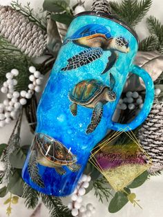 a blue coffee mug with sea turtles on it and pine cones in the background, surrounded by evergreen branches