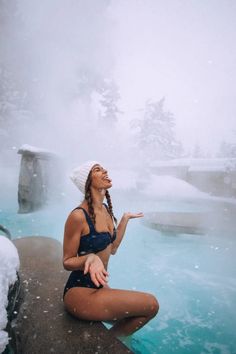 a woman in a bathing suit sitting on the edge of a blue pool with snow around her