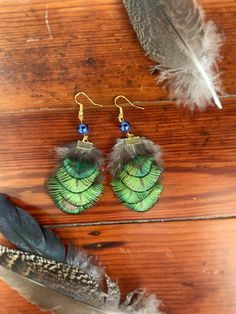 two green feathers and some beads on a wooden surface with a feather quill next to it