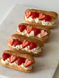 four sandwiches with strawberries and whipped cream on them sitting on a white counter top