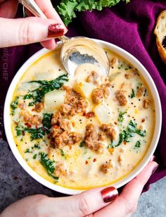 two hands holding a bowl of soup with meat and cheese