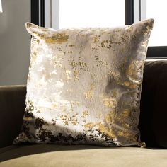 a gold and silver pillow sitting on top of a brown couch next to a window