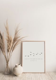 a white vase sitting next to a plant and a framed photo on a shelf in front of a wall