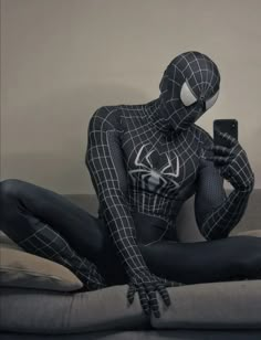 a spider man sitting on top of a bed holding a cell phone