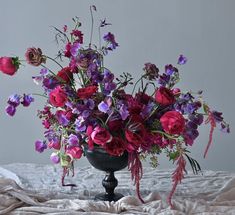 a black vase filled with lots of purple and red flowers on top of a bed