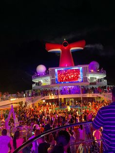 a crowd of people standing on top of a cruise ship at night with bright lights