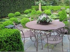 an outdoor table and chairs in the middle of a garden