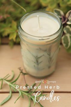 a candle sitting on top of a wooden table next to some leaves and flowers with the words, pressed herb candles