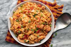 a white bowl filled with shrimp and rice on top of a table next to a spoon