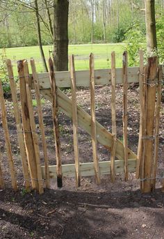 a fence made out of wood sticks in the dirt next to a tree and grass field