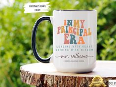 a black and white coffee mug sitting on top of a tree stump with the words, i am my principals era leading with heart building with vision