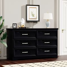 a black dresser sitting in a living room next to a lamp and pictures on the wall