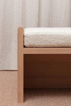 a wooden bench sitting on top of a carpeted floor next to a white curtain