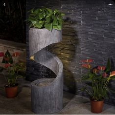 a water fountain with plants in it next to a brick wall and potted flowers