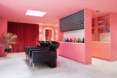 a room with pink walls and black chairs in it's center area, along with a bar that has bottles on the wall