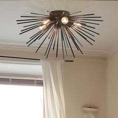 a chandelier hanging from the ceiling above a bed in a room with white curtains