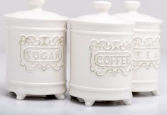 three white ceramic sugar jars sitting on top of each other with ornate designs and lettering