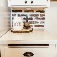 a cookie jar sitting on top of a white dresser next to a brick wall in a kitchen