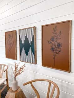 three framed art pieces hang on the wall next to a wooden chair and vase with flowers in it