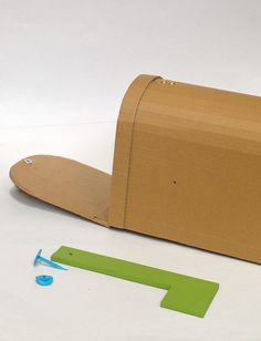 a cardboard box with a green piece of tape next to it on a white surface