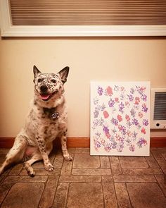 a dog sitting next to a painting on the floor