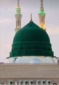 a large green dome on top of a building with two white minalis in the background