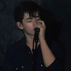 a young man holding a microphone up to his face while singing into a microphone in front of him