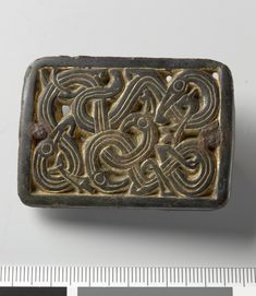 an old metal object with intricate designs on it's surface next to a ruler