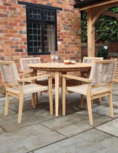 a wooden table and chairs on a patio with brick wall in the backround