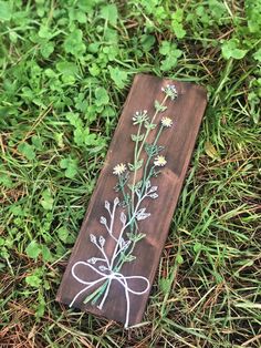 a piece of wood with flowers painted on it sitting in the grass next to some plants