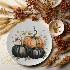 a plate with pumpkins painted on it next to some dried flowers and wheat stalks