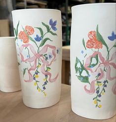 three vases painted with flowers on them sitting on a wooden counter top in front of a shelf