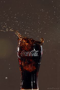 a coca - cola bottle splashing into the water on a dark background with bubbles