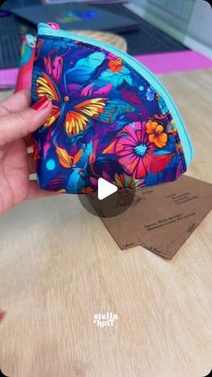 a hand holding a small colorful pouch on top of a wooden table