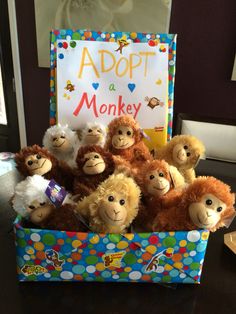 there are many stuffed animals in the box with a sign on it that says adopt a monkey