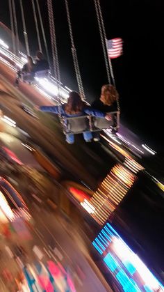 people riding on swings at night time in an amusement park with american flag hanging from the ceiling