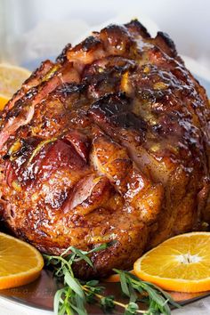 a ham with oranges and herbs on a plate next to some lemons,