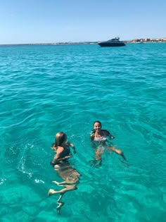 two people swimming in the ocean with a boat in the background