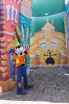 mickey mouse standing in front of some colorful buildings