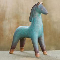 a small blue horse statue sitting on top of a cement floor next to a wall