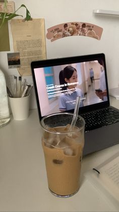 a laptop computer sitting on top of a desk next to a glass filled with liquid