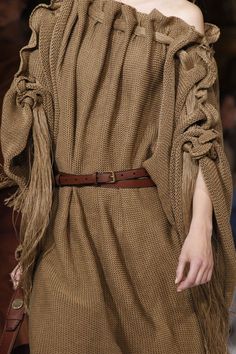 a woman walking down a runway wearing a brown dress with fringes on the sleeves