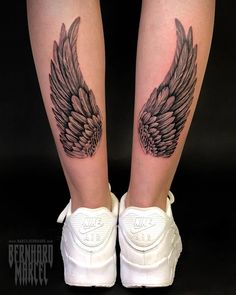 a pair of legs with black wings tattooed on the leg and white sneakers in front of them