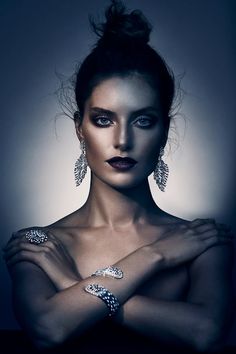 a woman with dark makeup and jewelry on her arm, posing for a photo in front of a black background