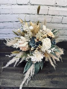 a bridal bouquet with feathers and flowers on a wooden table in front of a brick wall