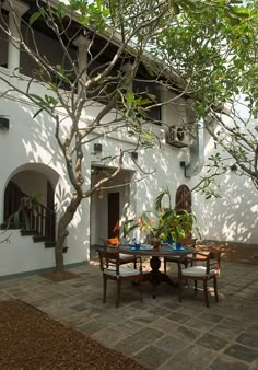 a table and chairs sitting under a tree in front of a white building with windows