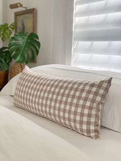 a bed with a checkered pillow on top of it next to a potted plant