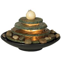 a water fountain with rocks and stones around it on a black plate against a white background